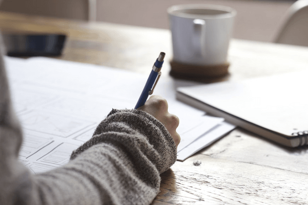 arm in grey sweater writing in notebook